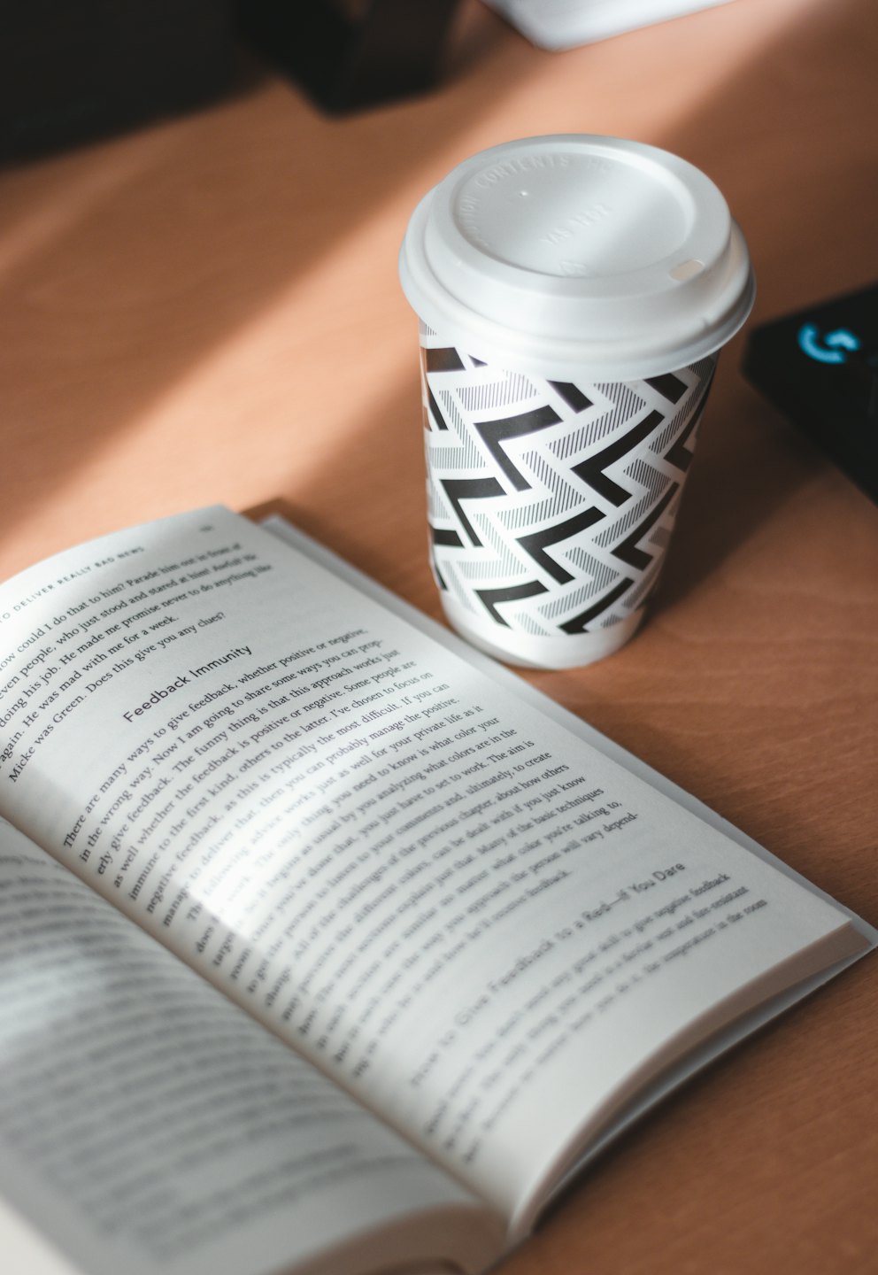 An open book lies on wood next to a patterned coffee cup.