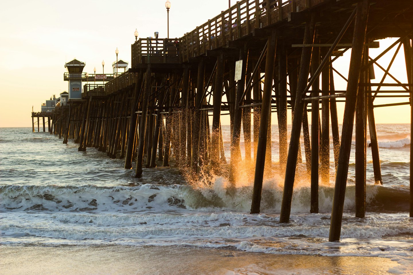 A wooden pier stretches out over crashing ocean waves.