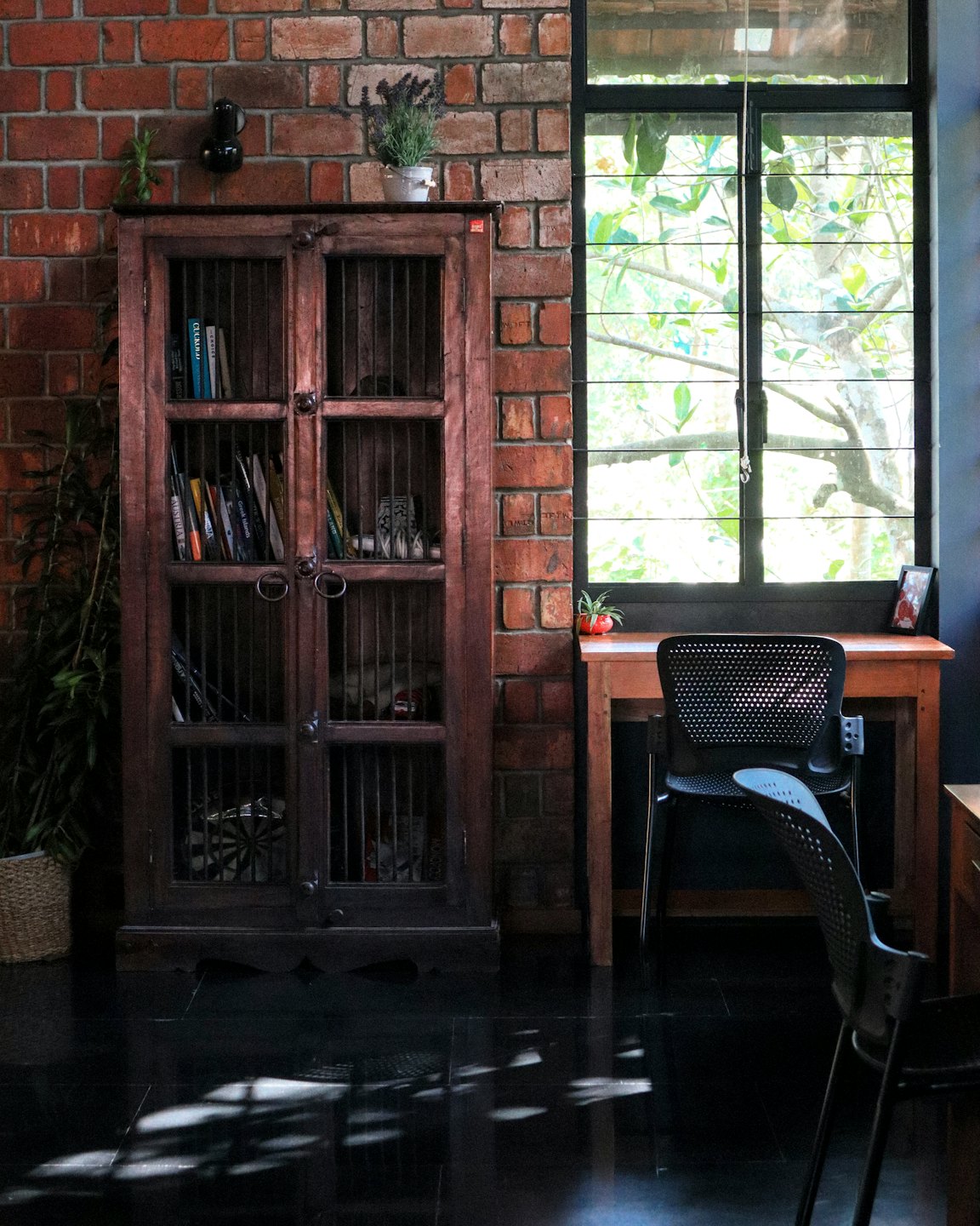 A wooden desk and chair sit beside a window with books.