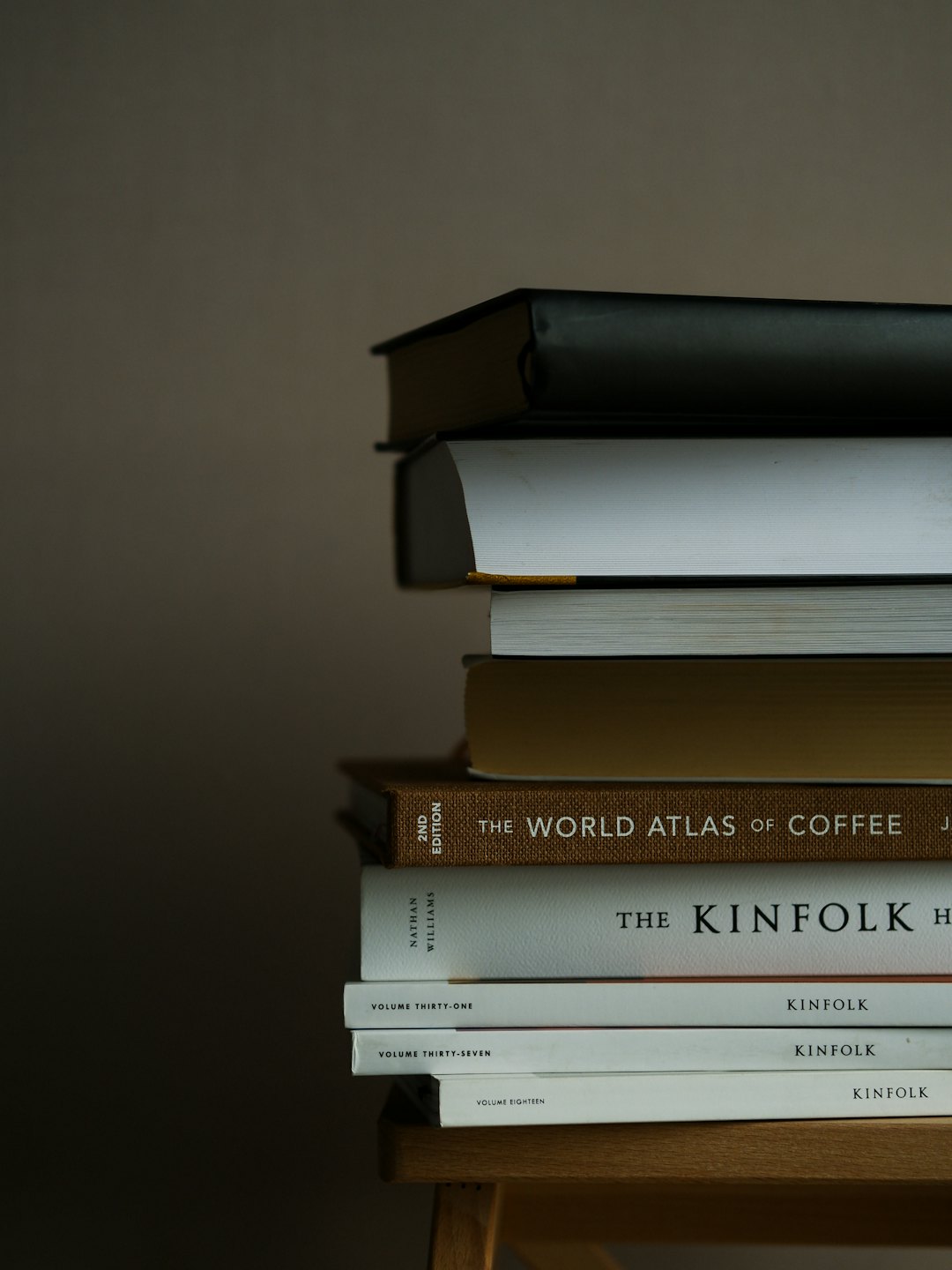 A stack of books on a light wooden table.